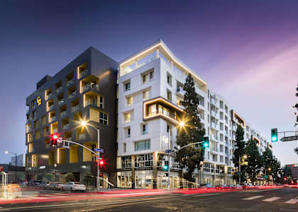 A modern building with a white and black facade stands on a street corner at dusk. at G12 Apartments, Los Angeles, CA, 90015