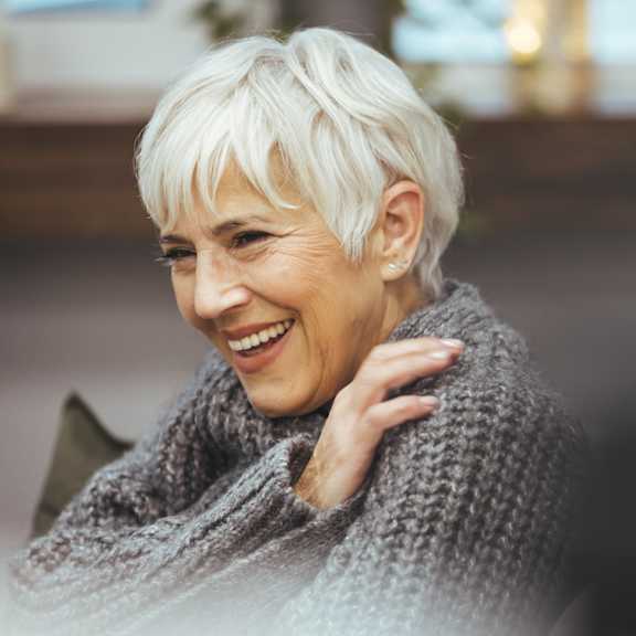 A woman with short white hair is wearing a grey sweater.