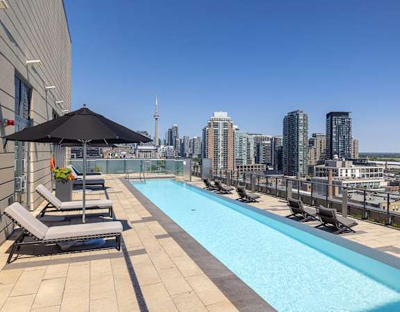 A rooftop pool with lounge chairs and umbrellas overlooking a city skyline.