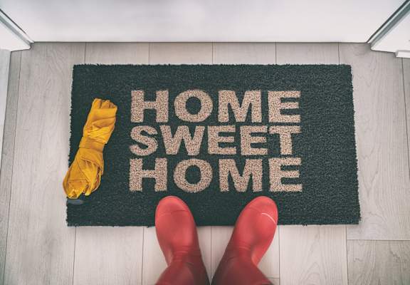 A pair of red boots are standing on a doormat that says "Home Sweet Home".