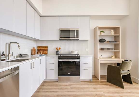 A modern kitchen with white cabinets and a wooden shelf.at WM by CLG, Los Angeles, CA