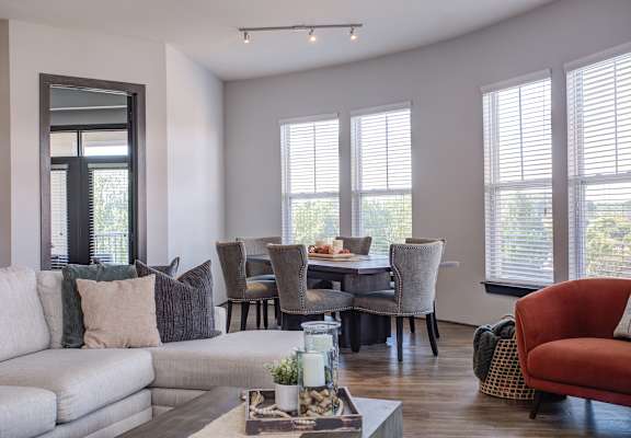 A living room with a grey couch, a red chair, and a dining table with chairs.
