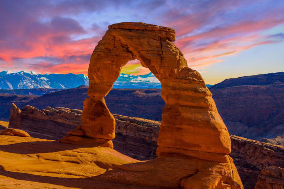 delicate arch with the mountains in the background at sunset