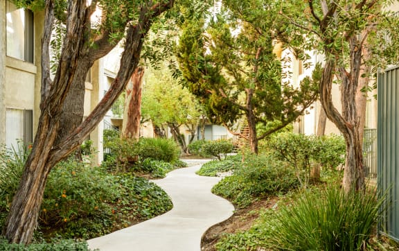 a walkway through trees and plants in an apartment building at Village Pointe Apartments, Northridge, CA, 91325