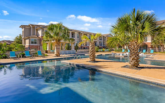 A large swimming pool surrounded by a grassy area and apartment buildings. at The Royce at 8100, Austin, TX, 78729
