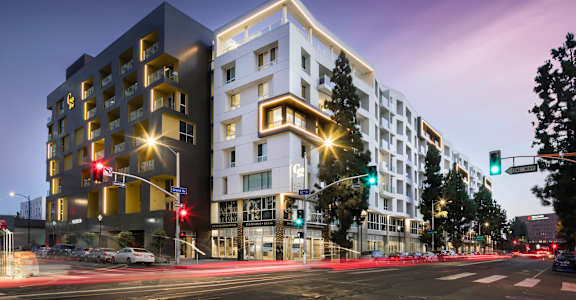 A modern building with a white and black facade stands on a street corner at dusk. at G12 Apartments, Los Angeles, CA, 90015