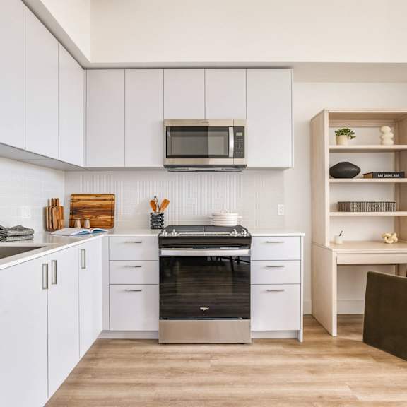 A modern kitchen with white cabinets and a wooden shelf.at WM by CLG, Los Angeles