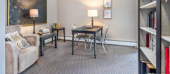 A living room with a grey couch, a table with a lamp, a chair and a bookshelf.