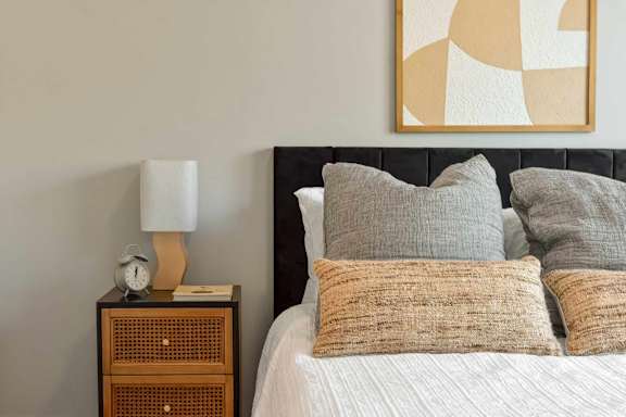A bed with pillows and a nightstand with a lamp and clock.