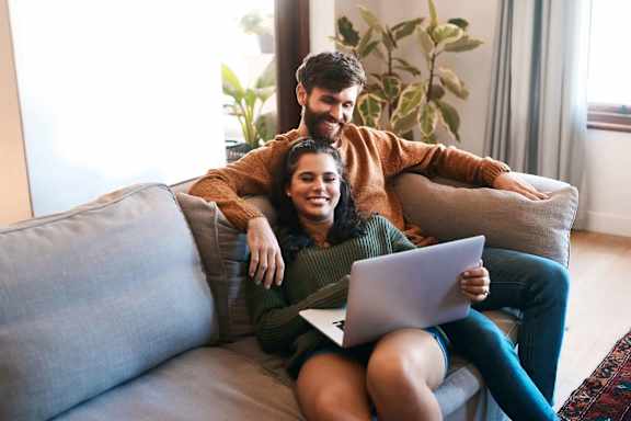 A man and woman are sitting on a couch with a laptop.