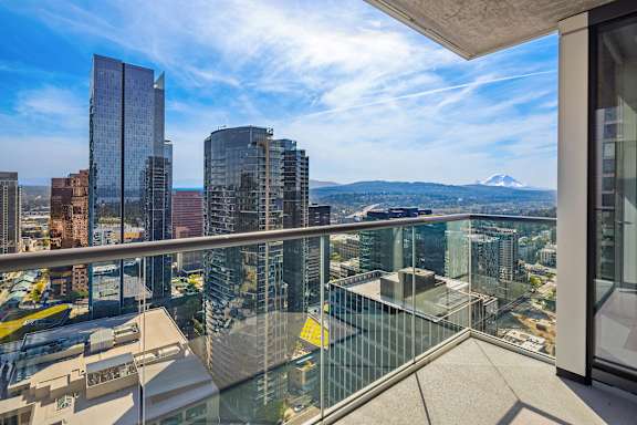 A glass balcony overlooks a cityscape with a mountain in the distance.