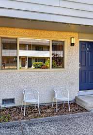 Two white chairs are placed on the concrete in front of a house.