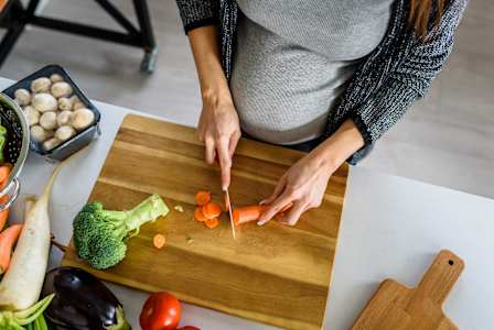 A person is cutting vegetables on a wooden cutting board.