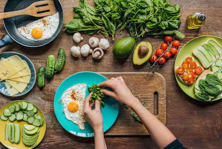 A person is preparing a meal with fresh vegetables and eggs on a wooden table.