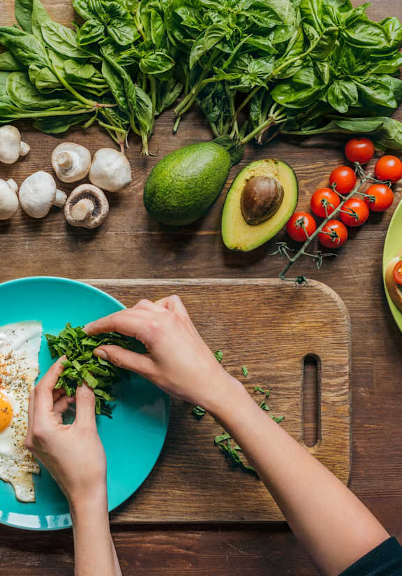 A person is preparing a meal with fresh vegetables and eggs on a wooden table.