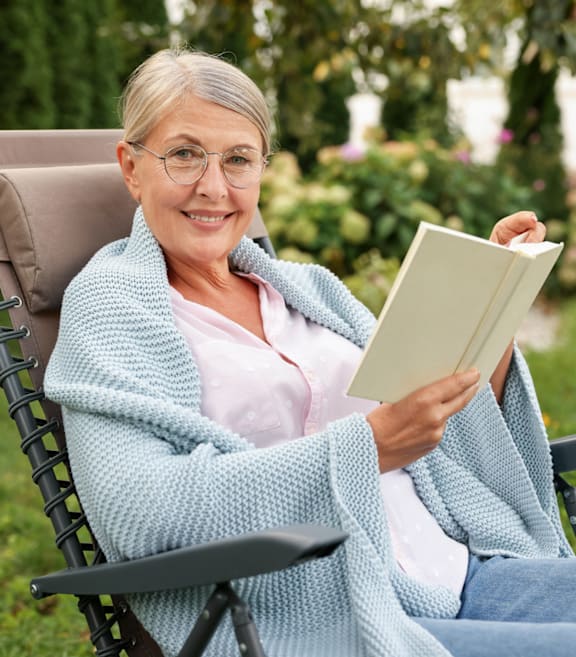 An elderly woman is sitting in a chair and reading a book.