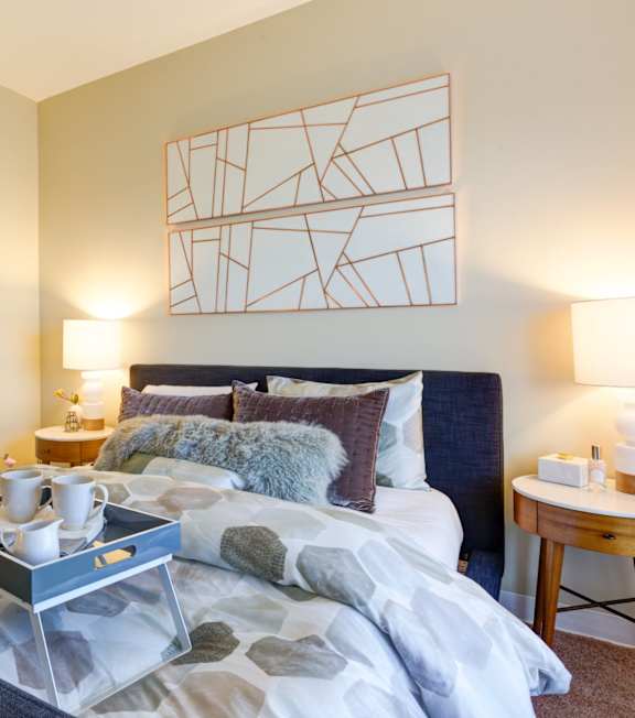 A bedroom with a bed, nightstand, and a painting on the wall.