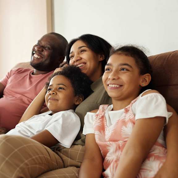 A family of four is sitting on a couch together.