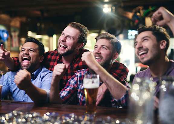 Four men are cheering and drinking beer in a bar.
