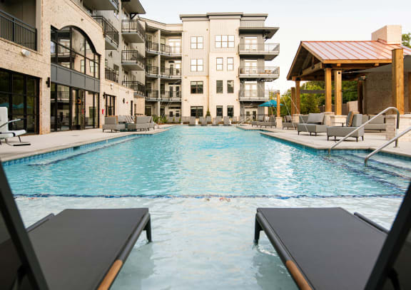 a swimming pool with lounge chairs in front of an apartment building at One Riverside Apartments, Chattanooga, TN, 37403