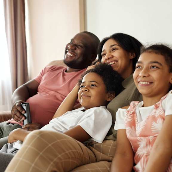 A family of four is sitting on a couch together.