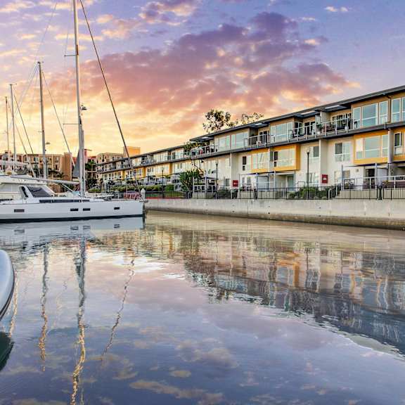 A boat is docked in front of a building with a sunset in the background.
