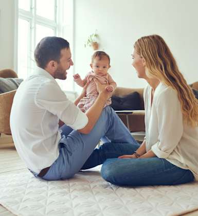 A family of three is sitting on the floor in a bright room.