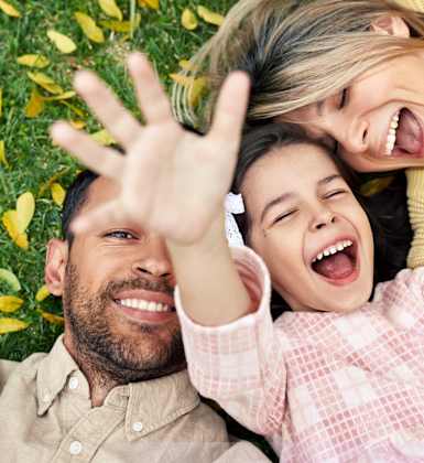 A family of three is lying on the grass with their hands in the air.