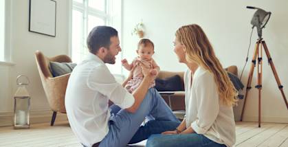 A family of three is sitting on the floor in a bright room.