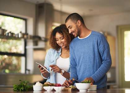 a man and woman standing in a kitchen looking at a cell phone