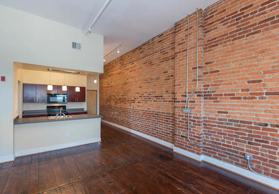 a living room with a brick wall and a kitchen at Mayton Transfer Lofts, Petersburg, VA 23803