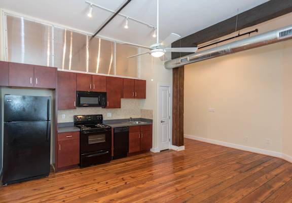 a kitchen with black appliances and wood floors at Mayton Transfer Lofts, Petersburg, VA 23803