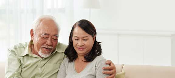 An elderly man and woman are sitting on a couch looking at a tablet.at Rosswood Villa Apartments, Santa Ana, CA