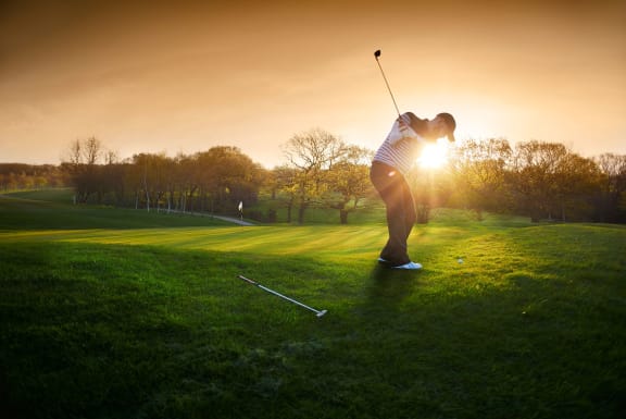 a woman playing golf on a golf course at sunset at District 2308, Arlington, 76011