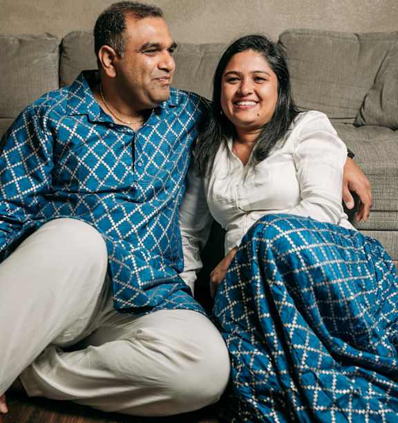 A man and a woman are sitting on the floor wearing matching blue and white checkered pajamas.