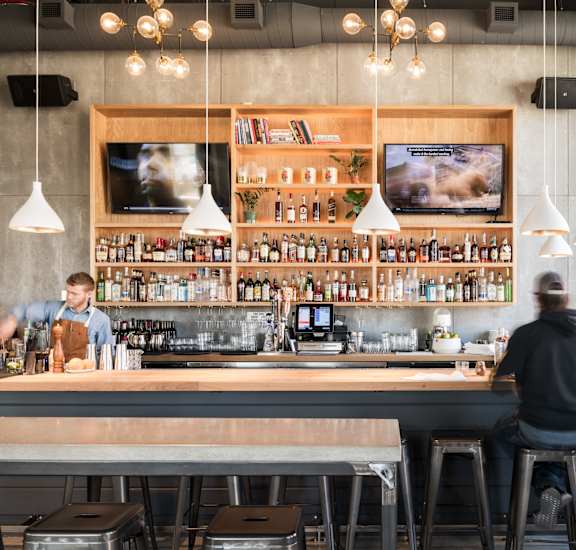 A man is sitting at a bar with a bartender behind the counter. at The Fowler Apartments, Boise, ID