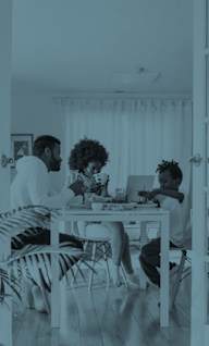 Three people sitting at a table in a room with white walls and plants.