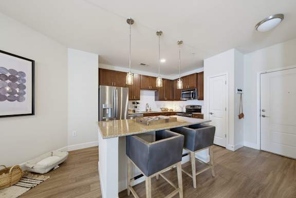 Kitchen island with two bar stools, a stainless refrigerator and range, dark wood cabinets, and three pendant lights.