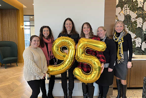Five women holding a number 95 balloon in a celebratory event.