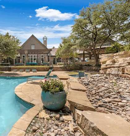 A large outdoor swimming pool surrounded by a stone wall and a large pot of flowers.