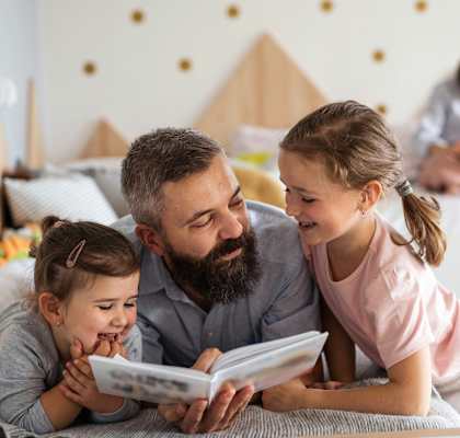 a father reading a book to his daughters on the bed at Parkside Apts, Pomona, 91766