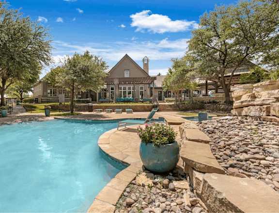 A large outdoor swimming pool surrounded by a stone wall and a large pot of flowers.