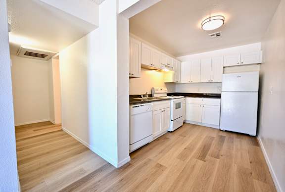 A kitchen with white appliances and wooden floors.