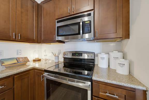 Stainless steel electric range and over-range microwave set against a white subway tile backsplash and wood cabinets.