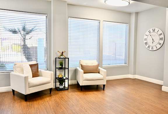 Two white chairs are placed in a room with a clock on the wall.