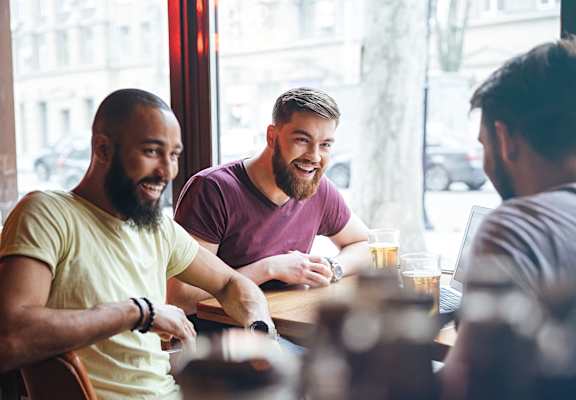 Three men are sitting at a table with drinks, engaged in conversation.