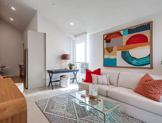 A modern living room with a white sofa, a glass coffee table, and a colorful abstract painting on the wall.