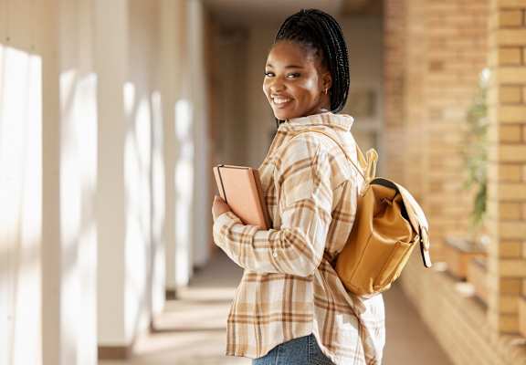 A person with a backpack and a book is standing in a hallway. at The Edge, Chico, California