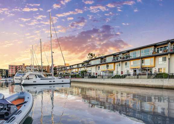 A marina with boats docked in front of a building with a sunset in the background at Marina Harbor, Marina del Rey, California
