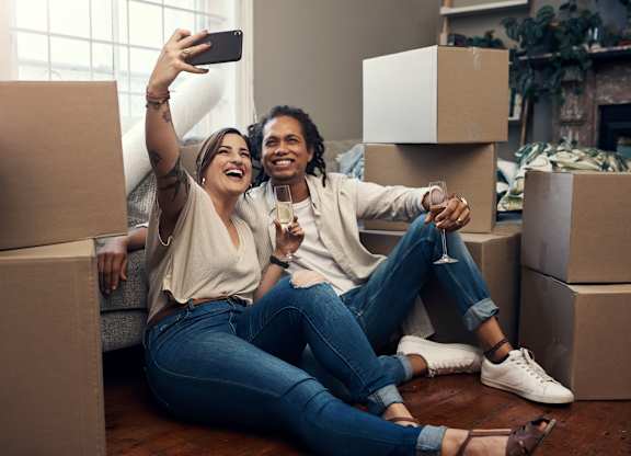 A couple is taking a selfie in their new home surrounded by moving boxes.at The Residences at The Gilmore in Gilbert, AZ